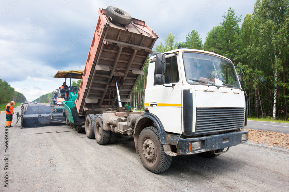 Lorry unloading asphalt into tracked paver during roadworks