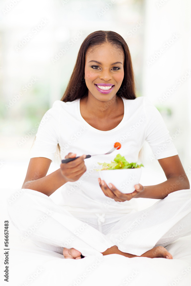 african american woman eating green salad in bed