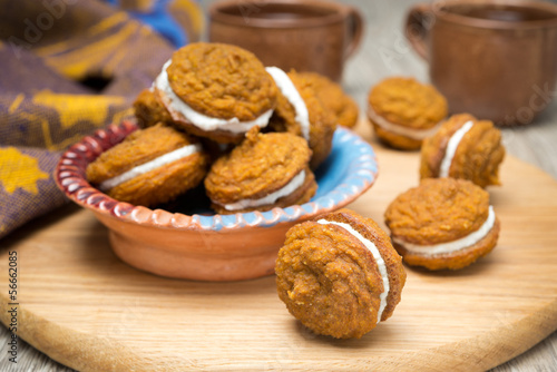 bowl of pumpkin cookies with cream filling on a wooden board