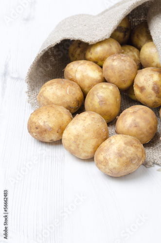 new potatoes in a sack on a white wooden board, vertical