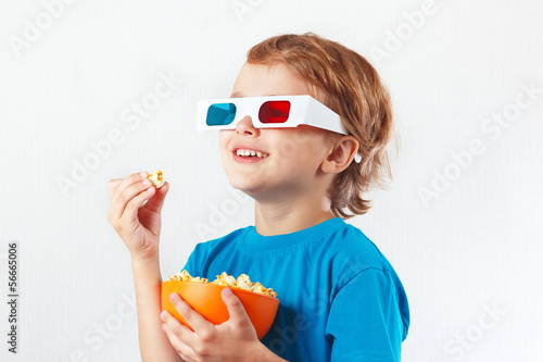 Young smiling boy in stereo glasses eating popcorn