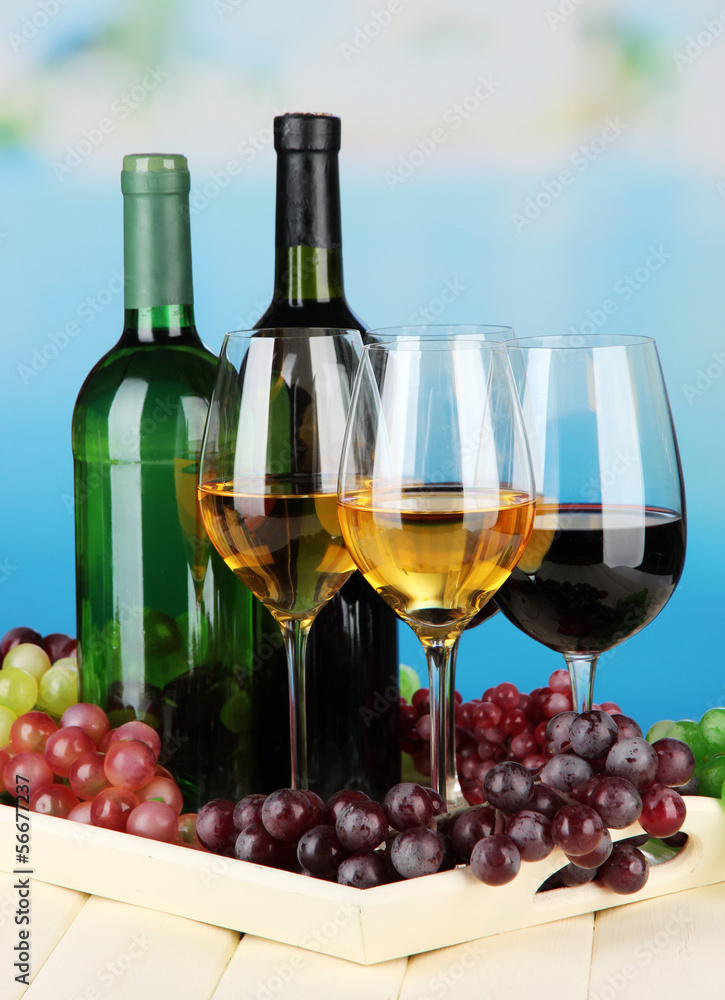 Wine bottles and glasses of wine on tray, on bright background