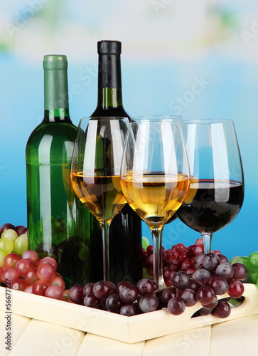 Wine bottles and glasses of wine on tray, on bright background