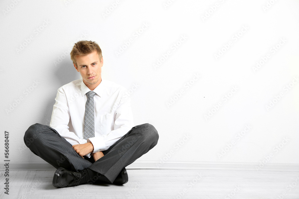 Young businessman sitting on floor, on gray wall background Young businessman sitting on floor, on gray wall background