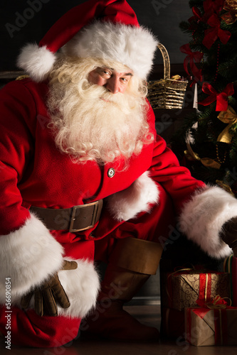 Santa placing gifts under Christmas tree in dark room