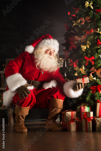 Santa putting gifts under Christmas tree in dark room