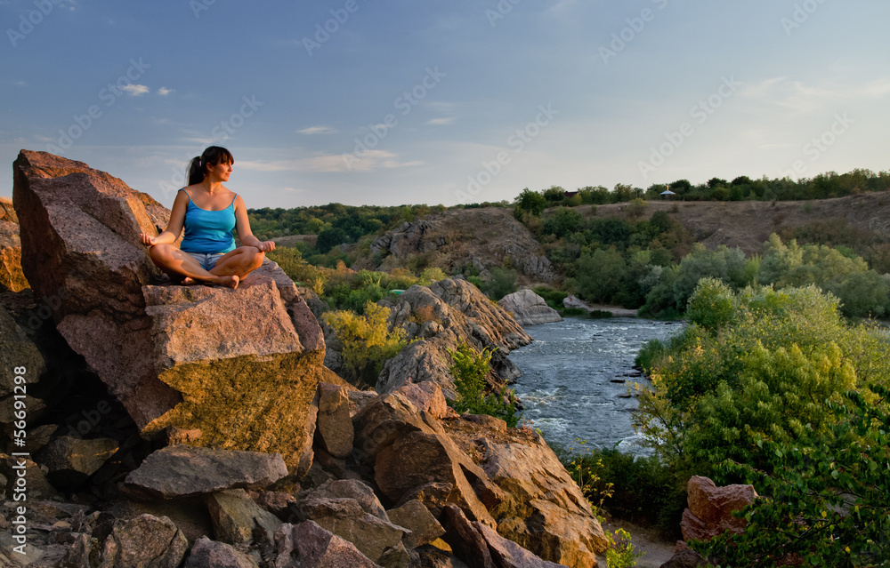 Woman meditating on a rock above a river