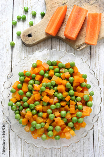 Boiled carrots with green peas in glass bowl