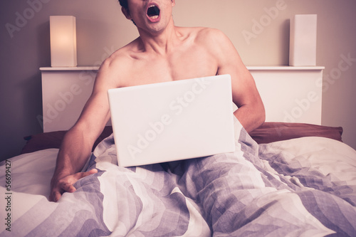 Young man is sitting in bed and watching pornography on laptop