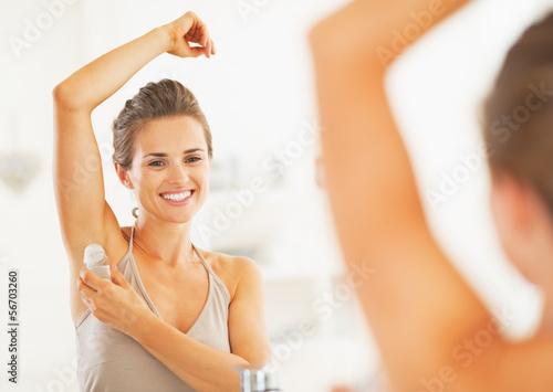 Canvas Print Smiling young woman applying roller deodorant on underarm