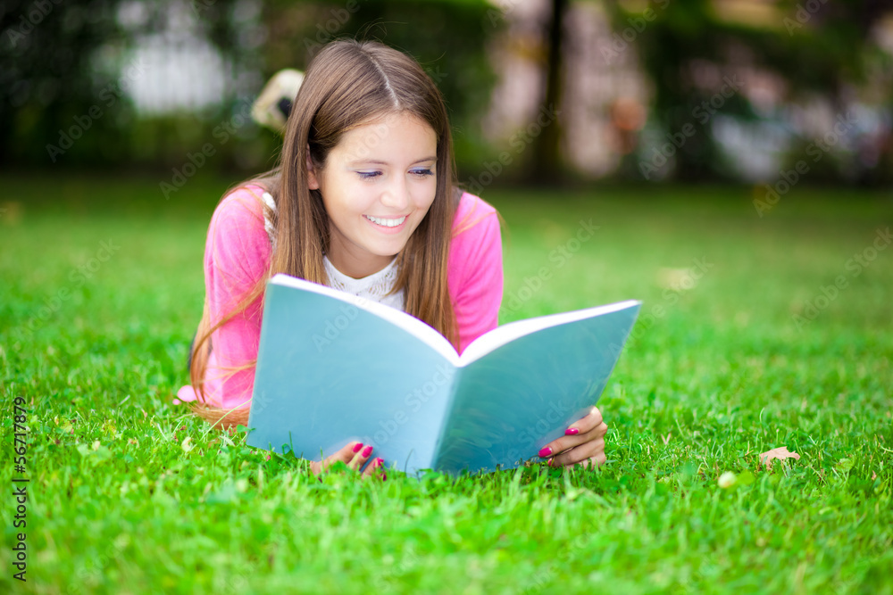 Fototapeta premium Young female student reading a book on the grass