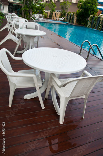 chairs and tables next to a swimming pool