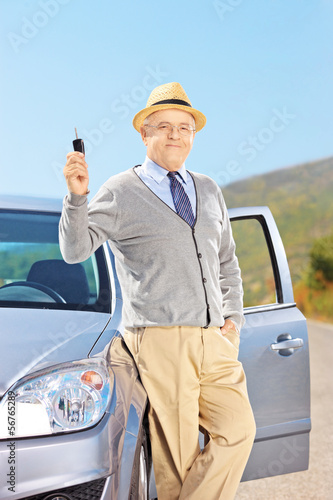 Smiling senior male holding a key next to his automobile outside