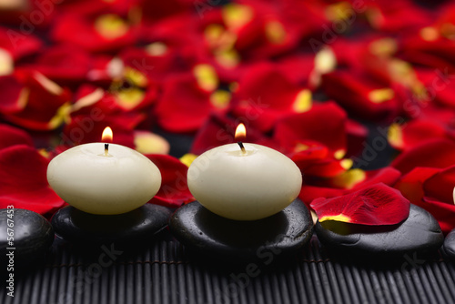 Stones with candle on mat with red rose petals