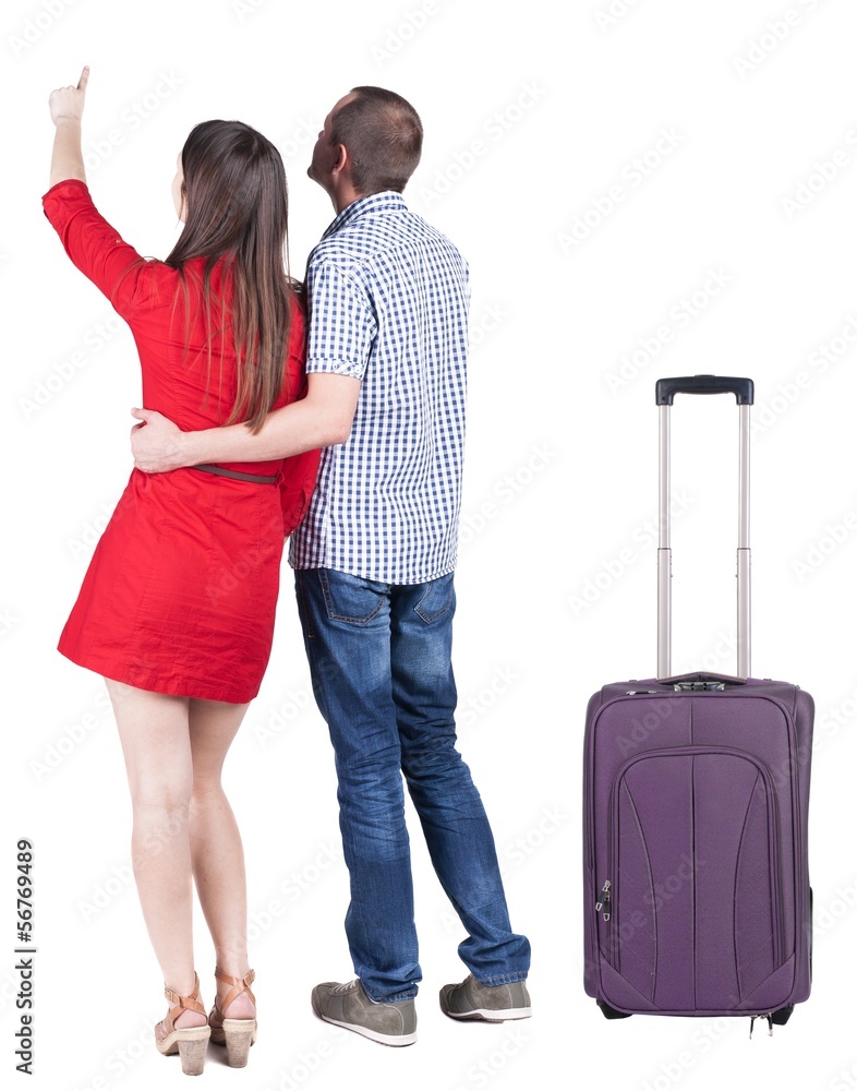 young traveling couple with suitcas pointing at wal. young traveling couple with suitcas pointing at wal.