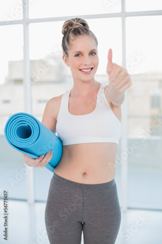 Sporty blonde holding balled up exercise mat giving thumb up