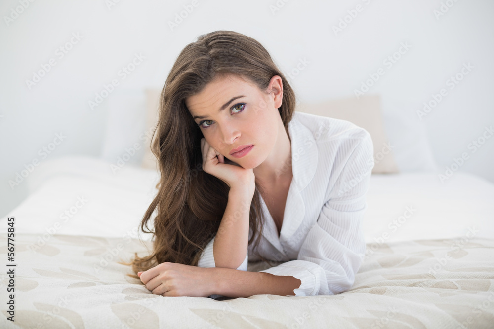 Troubled casual brown haired woman in white pajamas lying on her Troubled casual brown haired woman in white pajamas lying on her