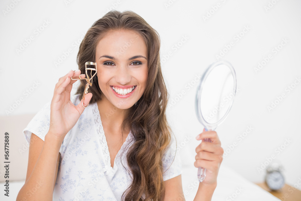 Smiling attractive brunette holding an eyelash curler and mirror Smiling attractive brunette holding an eyelash curler and mirror