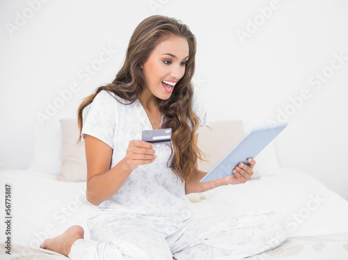 Surprised smiling brunette looking at tablet and holding credit