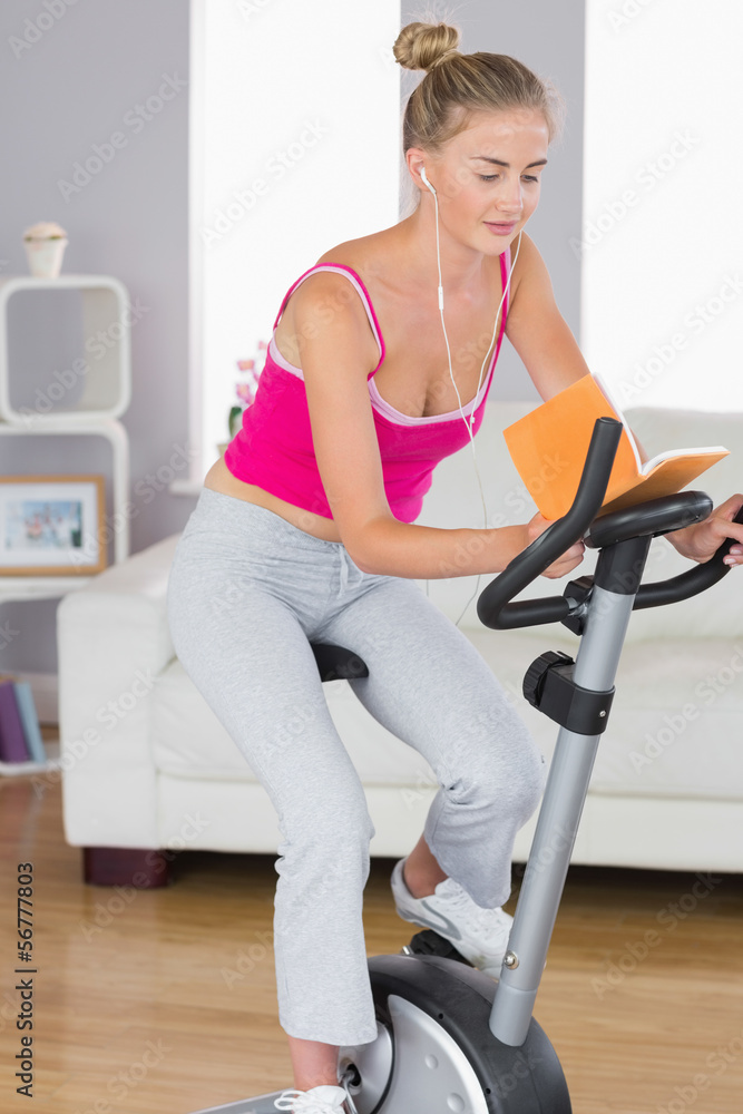 Sporty happy blonde training on exercise bike reading a book Sporty happy blonde training on exercise bike reading a book