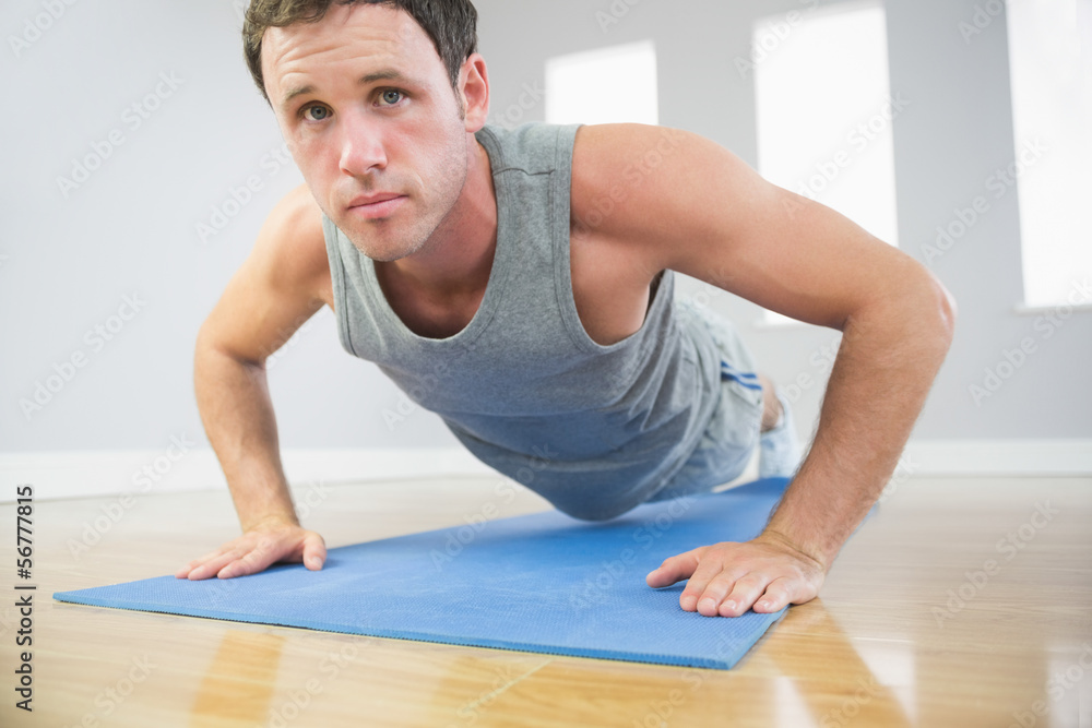 Attractive sporty man doing push ups on blue mat looking at came Attractive sporty man doing push ups on blue mat looking at came