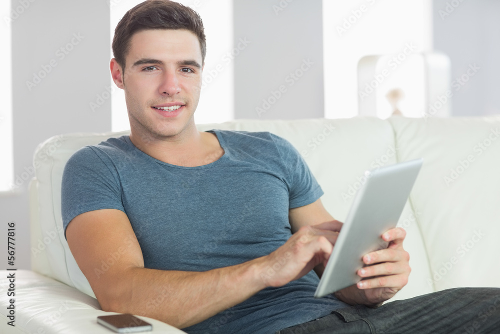 Smiling handsome man relaxing on couch using tablet Smiling handsome man relaxing on couch using tablet