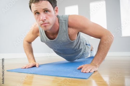 Attractive sporty man doing push ups on blue mat looking at came