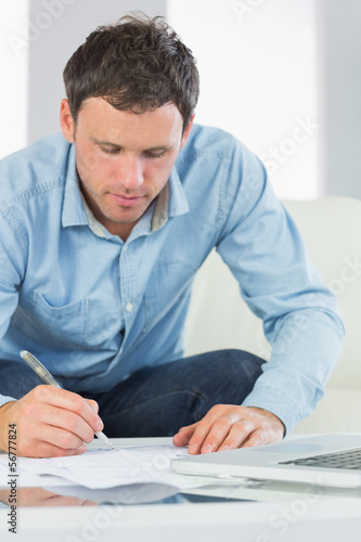 Content casual man writing on sheets paying bills
