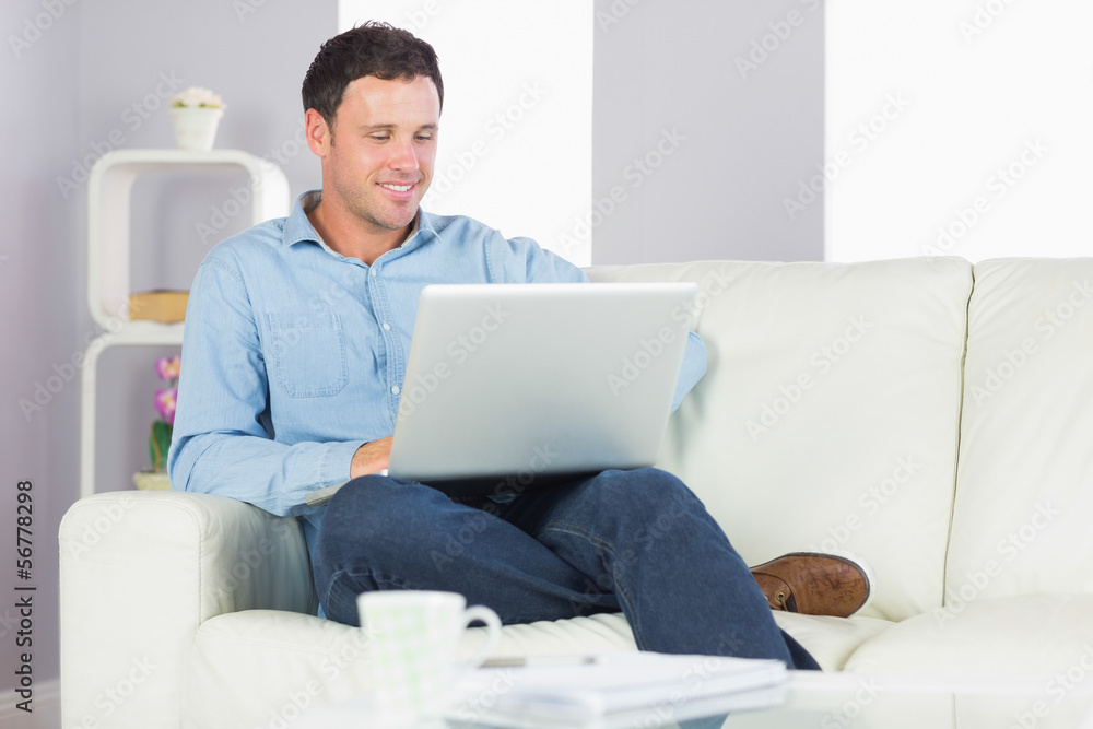 Content casual man sitting on couch using laptop Content casual man sitting on couch using laptop