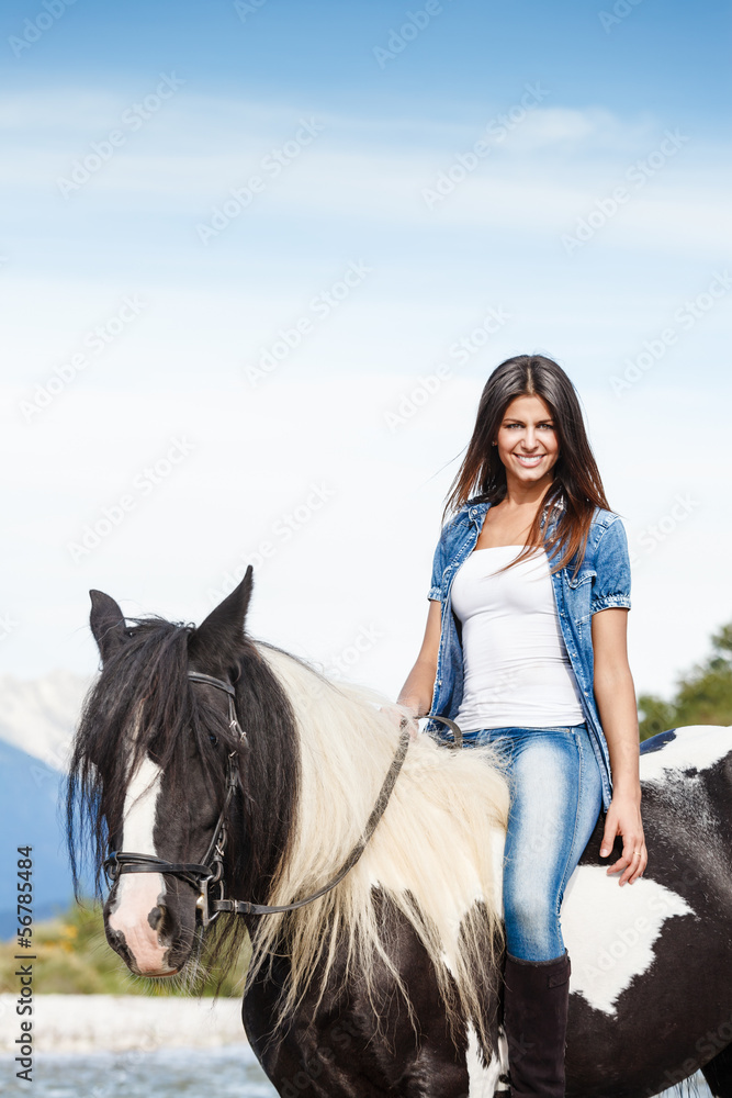 Fototapeta premium Attractive Young girl sitting on horse against blue sky