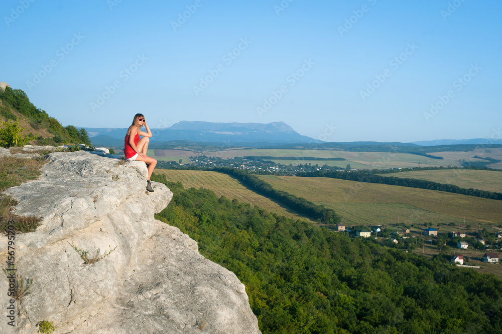 Smiling young woman sitting on the top of mountain
