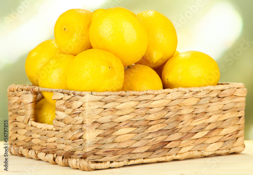 Ripe lemons in wicker basket on table on bright background