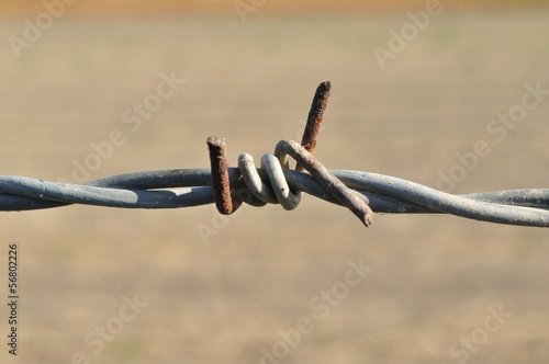 Rusty barbed wire against blurred brown background