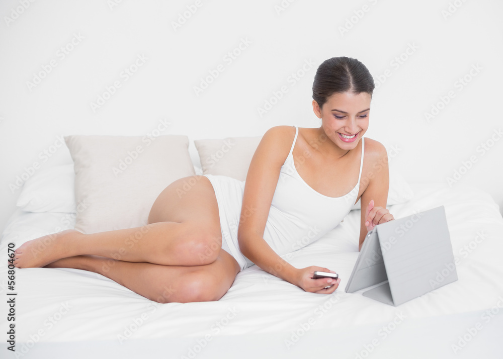Beautiful young brown haired model in white pajamas using a tabl Beautiful young brown haired model in white pajamas using a tabl