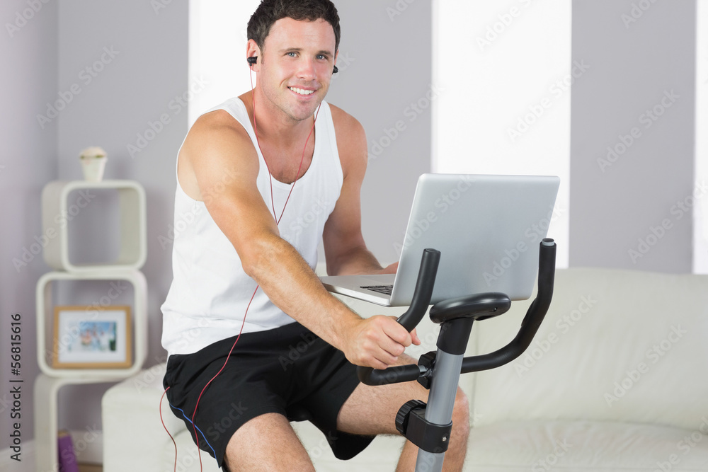 Sporty smiling man with earphones exercising on bike and holding Sporty smiling man with earphones exercising on bike and holding