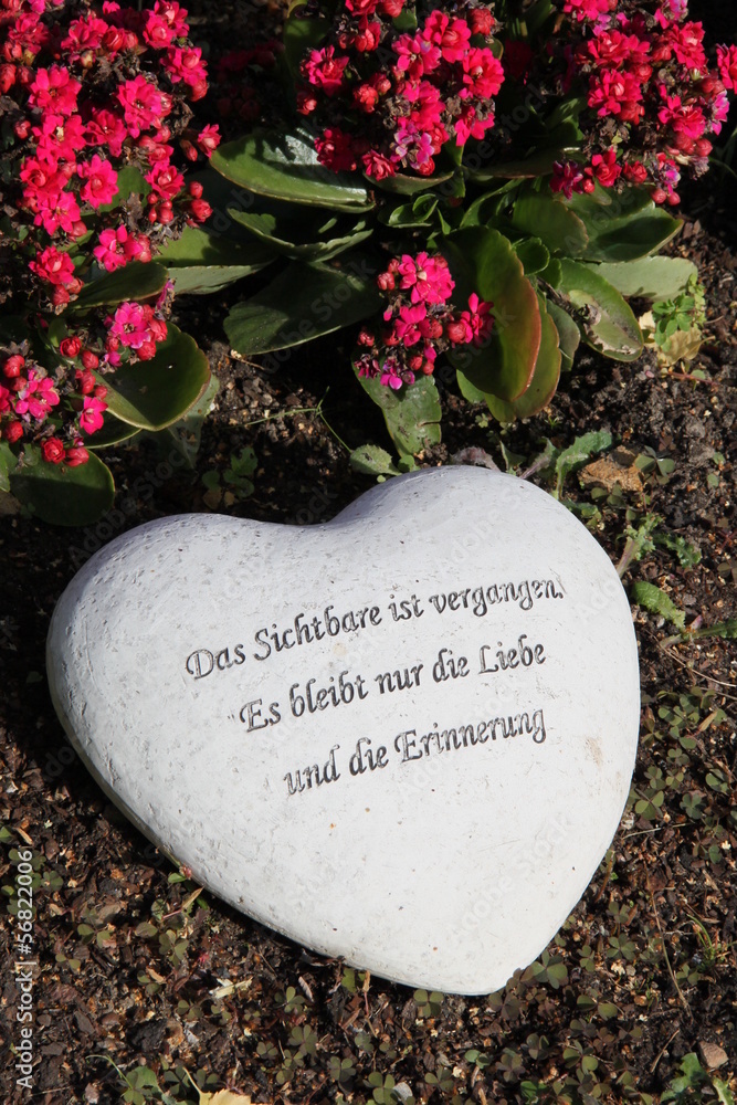 Herz mit Trauerspruch neben Blumen auf einem Grab StockFoto Adobe Stock
