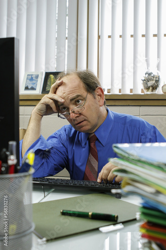 Tired and frustrated businessman at desk, vertical
