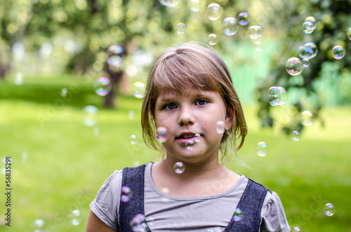 Little girl playing with soap bubbles in summer park
