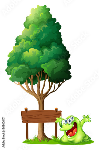 A happy green monster beside the empty wooden signage under the