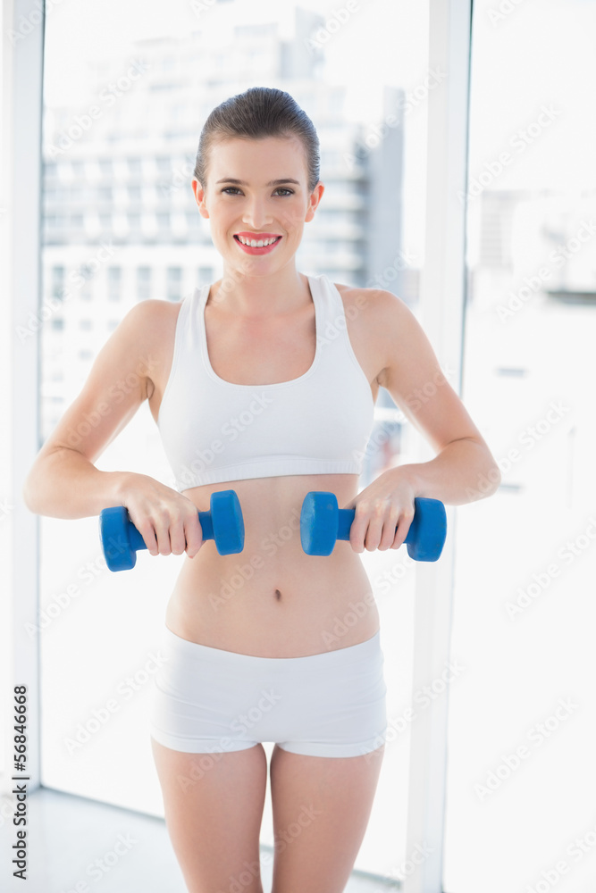 Smiling fit brown haired model in sportswear exercising with dum