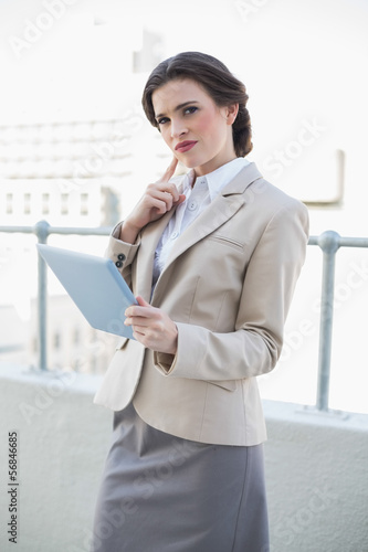 Thinking stylish brown haired businesswoman holding a tablet pc