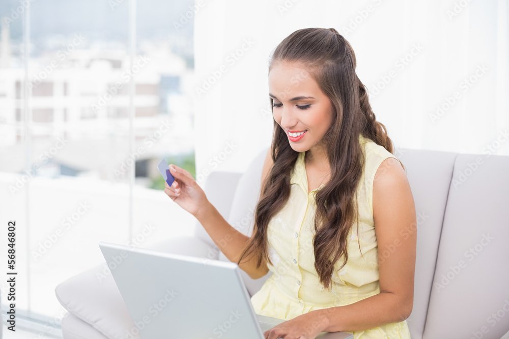 Smiling young brunette using credit card and laptop Smiling young brunette using credit card and laptop