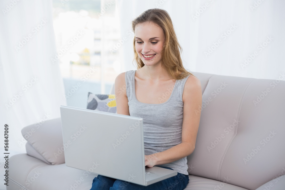 Cheerful young woman sitting on couch using laptop Cheerful young woman sitting on couch using laptop