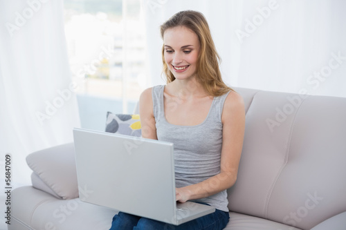 Cheerful young woman sitting on couch using laptop