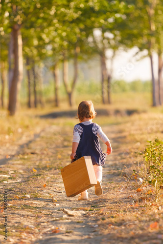 Sweet little girl playing with suitcase on the country road