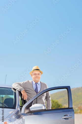 Confident mature gentleman with hat posing next to his car
