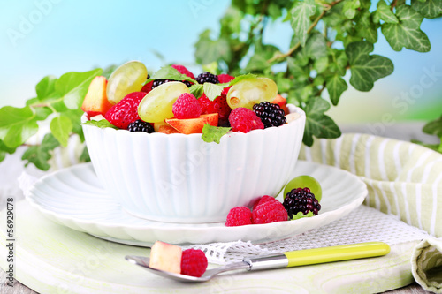 Fruit salad in bowl, on wooden table, on bright background