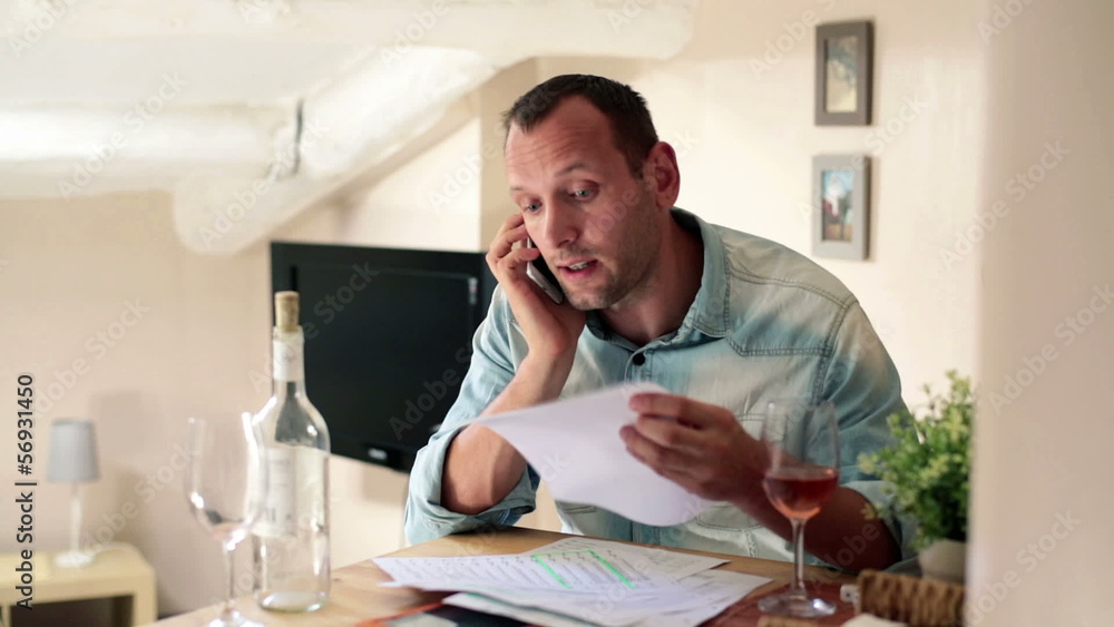 Unhappy, sad man with bills talking on cellphone at home Unhappy, sad man with bills talking on cellphone at home