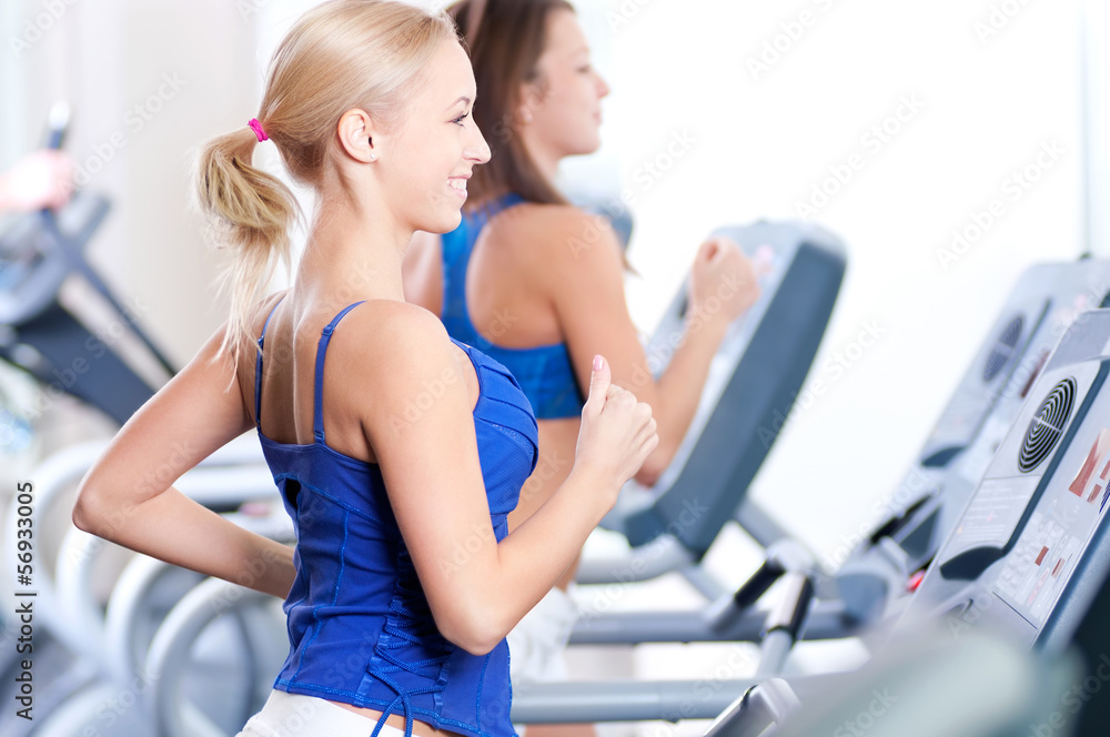 Two young women run on machine in the gym