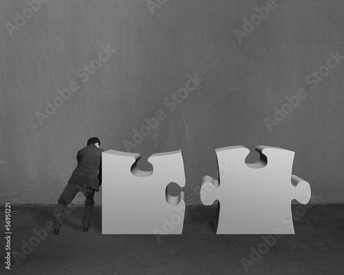 Businessman push two heavy puzzles together in concrete wall bac